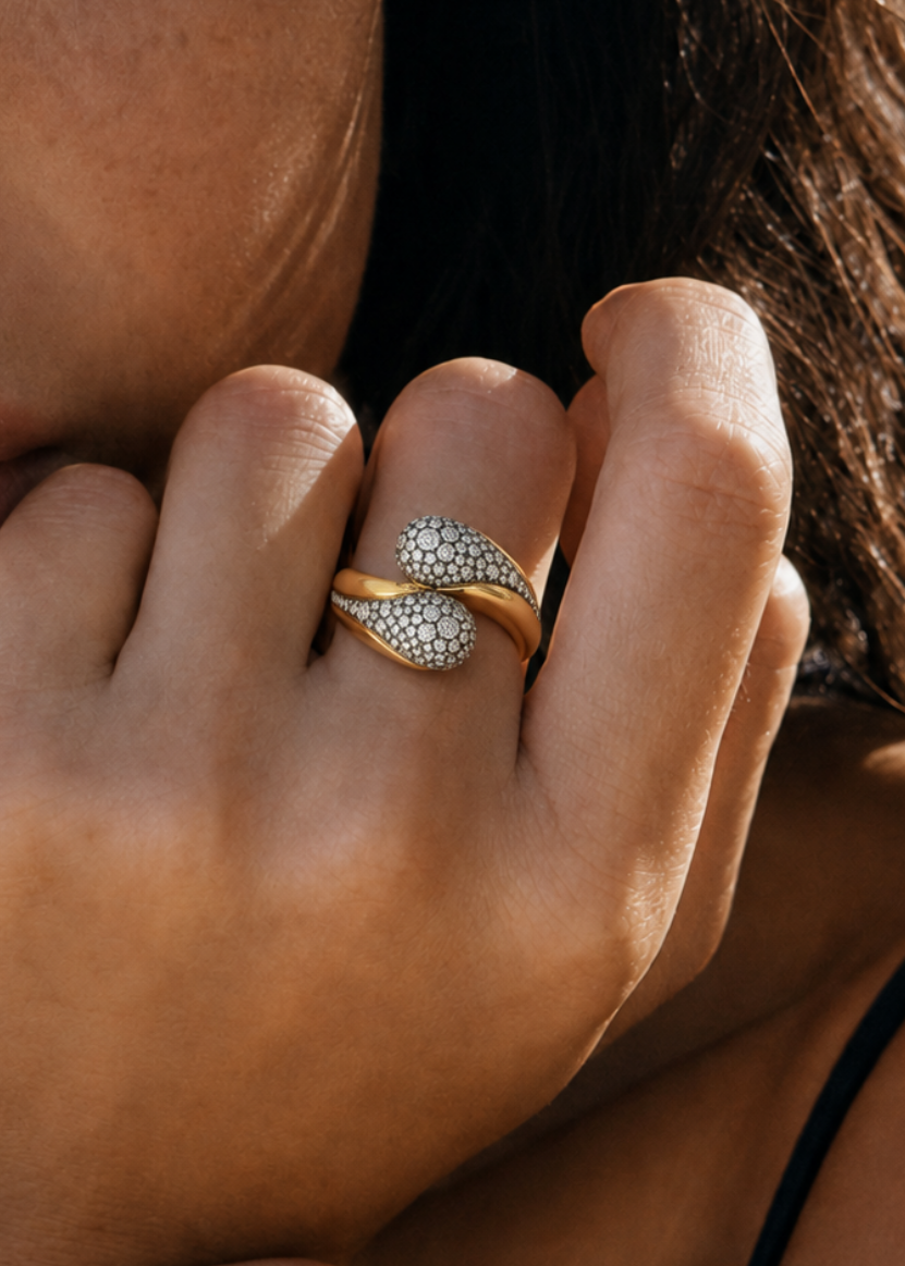 Close-up of a model wearing a sculptural yellow gold ring with pavé-set rounded ends