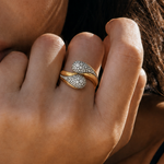 Close-up of a model wearing a sculptural yellow gold ring with pavé-set rounded ends